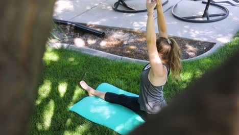 Slow-motion-shot-panning-from-behind-a-tree-and-revealing-a-woman-doing-yoga-on-a-yoga-mat