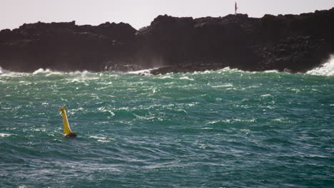 Waves-breaking-onto-rocks-while-ocean-swirls-around-below