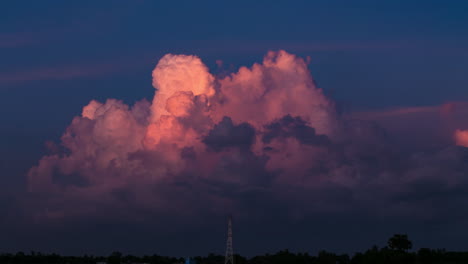 Cloud-formations-at-sunset,-bubbling-in-the-last-red-light-of-the-day-over-a-electricity-pylon,-during-south-east-Asia-monsoon-season
