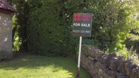 Static-Shot-of-British-‘For-Sale’-Real-Estate-Sign-on-Sunny-Summer’s-Day-with-Foliage-Blowing-in-the-Breeze-in-the-Background