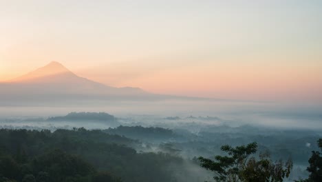 Sun-ricing-over-Mount-Merapi,-overlooking-the-Buddhist-temple-Borobudur,-lost-in-the-early-morning-swirling-mist