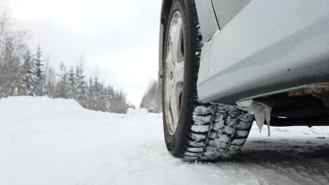 Static-low-angle-close-up-shot,-car-wheels-spinning-on-snowy-winter-road,-in-Rovaniemi,-Finland