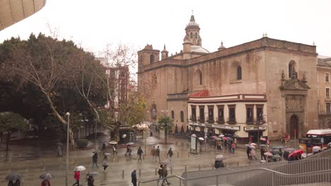 People-walk-past-church-in-rainy-Seville,-seen-from-Las-Setas-stairs