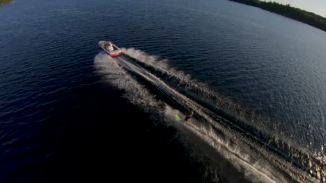Zeitlupe---Kaukasischer-Mann-Slalomt-Wasserski-Vom-Weißen-Boot-Auf-Blauem-See-Im-Sommerabendlicht,-FPV-Drohnen-Luftorbit-Folgt