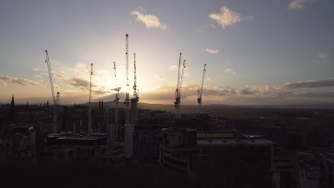 Revealing-shot-of-the-city-of-Edinburgh-with-wonderful-sunset-light-and-clouds-in-Scotland-and-with-cranes-in-the-shot-taken-from-Calton-hill
