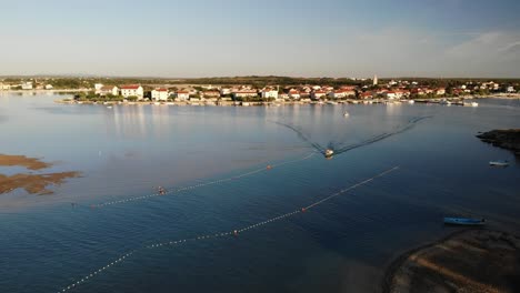 Aerial-panorama-of-a-Nin-town-with-lagoon-and-boat-approaching-narrow-pathway-in-sunset