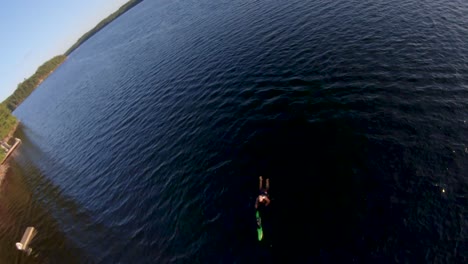 Die-Hüttenfamilie-Fährt-Nach-Dem-Wasserskifahren-Mit-Dem-Boot-Zum-Dock,-Ein-Mann-In-Schwimmweste-Schwimmt-Bei-Sommerlichem-Sonnenuntergang-Zum-Ufer-Im-Blauen-See