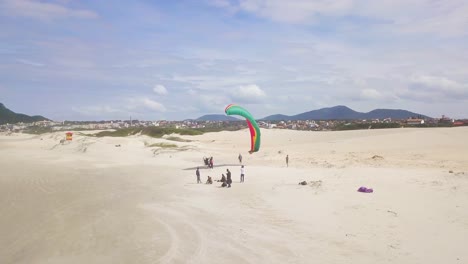 4K-Aerial-Shot-of-Paramotor-Opening-its-Wings-on-the-Beach-with-People-Around