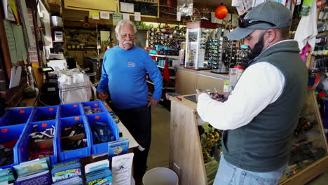 Caucasian-male-with-beard-buys-fishing-tackle-from-man-at-store-counter,-medium-shot