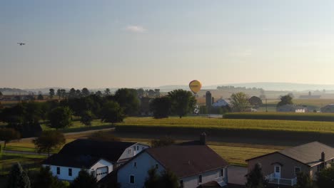 Aerial-dolly-forward-toward-Meineke-hot-air-balloons,-Powered-Paraglider-crossing-sky-in-Amish-Country-with-farms-and-buildings
