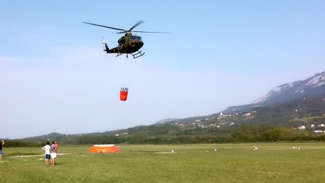 Hubschrauber-Mit-Eimer-Holen-Wasser-Zur-Bekämpfung-Eines-Waldbrandes,-Feuerwehrleute-Mit-Lastwagen-Leisten-Bodenunterstützung
