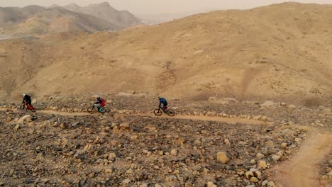 Group-of-Filipino-mountain-bikers-cycling-downhill-enduro-on-the-Al-Taween-trail-of-Shawka-Showka,-Ras-Al-Khaimah,-United-Arab-Emirates