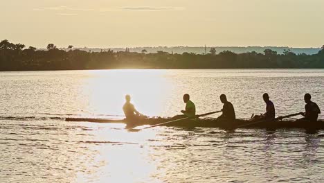 Silhouette-male-rowing-team-practising-in-shimmering-sunset-lake-water-reflections