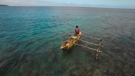 Vanuatu-Island,-Local-Male-Sitting-on-Boat-With-Outrigger-and-Holding-Fishing-Net,-Static-Aerial-View