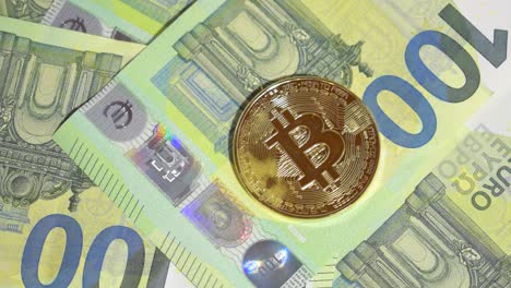 Male-Hand-Laying-Down-Hundred-Euro-Banknote-And-Single-Golden-Bitcoin-On-Stack-Of-Hundred-Euro-Banknotes
