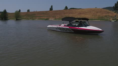 Aerial-view-orbiting-speed-boat-floating-on-calm,-quiet-lake-ready-for-water-skier