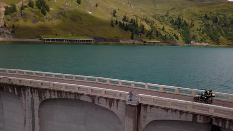 Lake-Fedaia-Dam-at-Dolomite-mountains-with-motorbike-and-car-traffic-above-the-wall-road,-Aerial-Drone-orbit-reveal-shot