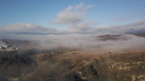 Aerial-view-of-fine-mist-over-rural-land-outside-small-town,-zooming-shot