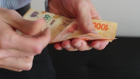 Young-businessman-counting-Argentine-cash-money-"pesos".-Close-up