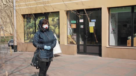 A-woman-in-an-anti-virus-mask-and-gloves-is-standing-in-a-queue-in-front-of-the-store