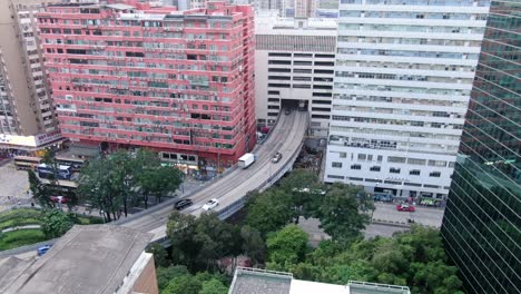 Traffic-passing-through-a-Car-park-building-in-downtown-Hong-Kong,-with-city-mega-buildings,-Aerial-view