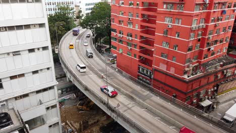 Traffic-passing-through-a-Car-park-building-in-downtown-Hong-Kong,-with-city-mega-buildings,-Aerial-view