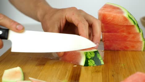 Slicing-the-green-rind-off-a-juicy-watermelon,-on-a-wooden-chopping-board