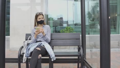 Una-Joven-Con-Mascarilla-Sentada-En-Una-Estación-De-Autobuses-Esperando-En-El-Transporte-Público