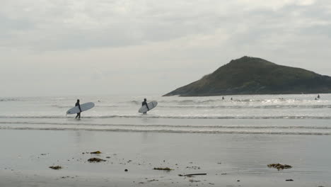 Surfers-wading-out-into-ocean-waves-in-slow-motion