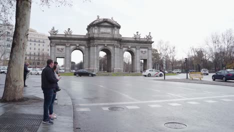 Menschen,-Die-Darauf-Warten,-Die-Straße-Zu-überqueren,-Während-Fahrzeuge-Auf-Der-Straße-In-Der-Nähe-Der-Puerta-De-Alcala-Auf-Der-Plaza-De-La-Independencia,-Madrid,-Spanien,-Fahren