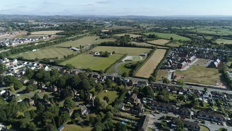 Aerial-of-the-village-of-Topsham,-residential-estate-sports-grounds-and-fields-make-up-the-foreground