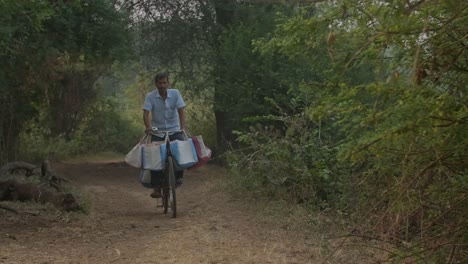 Indischer-Mann-Auf-Einem-Fahrrad,-Der-In-Zeitlupe-Auf-Unbefestigten-Dorfstraßen-Fährt