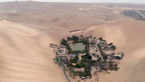 Aerial-view-above-the-small-village-of-Huacachina-Peru,-A-small-village-around-a-desert-oasis-surrounded-by-sand-dunes