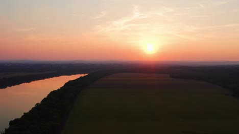 Drone-flying-parallel-to-orange-river-waters-tinted-by-the-amazing-sun-setting-though-the-clouds-on-horizon-maryland-usa