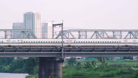 A-Model-N700-Shinkansen-Bullet-Train-Passing-Over-A-Bridge-At-The-Tamagawa-River-With-Skyscrapers-At-The-Background-In-Tokyo,-Japan---Tripod-Shot