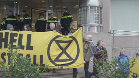 Grupo-De-Activistas-Que-Muestran-Una-Gran-Pancarta-Que-Dice-&quot;el-Proyectil-Debe-Caer&quot;-Protestando-Frente-A-La-Sede-Del-Proyectil-Real-Holandés-En-La-Haya---Plano-Medio,-Giro-A-La-Derecha