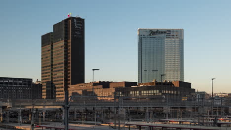 Trenes-En-La-Estación-Central-De-Oslo-Con-Postgirobygget-Y-El-Hotel-Radisson-Blu-Plaza-Al-Fondo-Al-Atardecer-Del-Proyecto-De-Código-De-Barras-En-Oslo,-Noruega