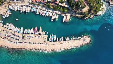 Close-up-drone-flight-over-the-water-surface-of-the-yacht,-boats-and-cars-in-the-background-of-the-resort-town-located-between-the-green-hills