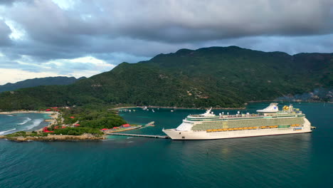 Wide-drone-shot-of-cruise-ship-docked-in-the-Haiti-with-coastal-mountains-in-the-background