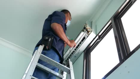 Yogyakarta,-Indonesia---Mar-1,-2021-:-A-man-checking-and-repairing-an-air-conditioner-or-ac-machine-near-a-window