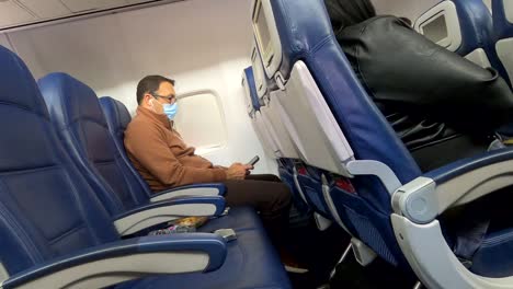 Middle-aged-Caucasian-man-scrolling-cellphone-with-mask-on-while-waiting-on-flight-to-take-off