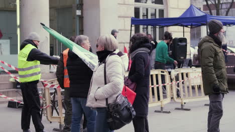 Mann-Mit-Italienischer-Flagge-Und-Sicherheitsmänner-In-Der-Nähe-Von-Menschen,-Die-Auf-Der-Piazza-XXV-April-Für-Freiheit-Und-Wahrheit-In-Mailand,-Italien,-Gegen-Die-Regierung-Protestieren