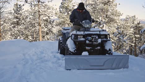 Ein-Kaukasischer-Mann-Setzt-Sich-Auf-Ein-Geländefahrzeug-Oder-Ein-Geländewagen-Mit-Pflug-Und-Fährt-Vorwärts,-Um-Den-Schnee-Von-Einer-Bergauffahrt-Zu-Räumen