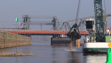 Corredor-Fluvial-Que-Conduce-Debajo-De-Un-Puente-Sobre-El-Río-Ijssel-En-El-Fondo-Con-Maquinaria-Pesada-Dragando-Un-Barco-En-Primer-Plano-En-El-Trabajo