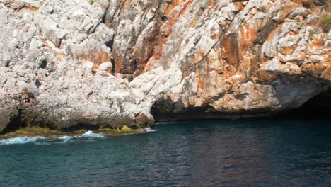 View-of-underwater-cave-entrance,-Alanya-,-red-cliff,-blue-sea-watter,-handheld-medium-shot-from-a-boat
