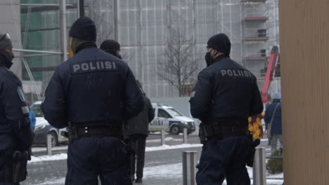 A-medium-shot-of-a-few-armed-police-officers-standing-on-the-streets-of-Helsinki-during-covid-protests,-wearing-masks