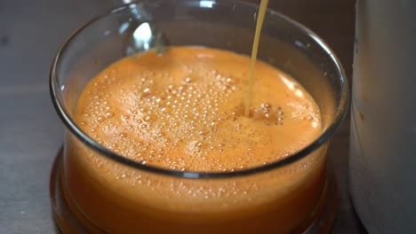 Fresh-carrot-and-orange-juice-poring-down-into-glass-bowl-from-juice-machine---Slow-motion