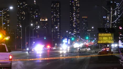 Police-cars-with-siren-lights-on-near-a-car-accident,-behind-a-caution-yellow-tape,-at-night