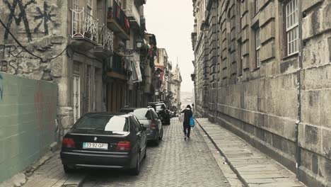 Hombre-Cargando-Bolsas-A-Través-De-Una-Calle-Lateral-Vieja-Y-Vacía-En-La-Ciudad-De-Portugal-Porto