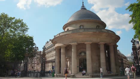 Panning-across-rotunda-main-entrance-with-people-walking-by-and-skaters-skating-on-sunny-summer-day-in-Parc-Monceau-in-Paris,-France